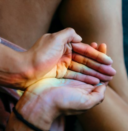 hands making a cup shape with a reflection of a rainbow over it